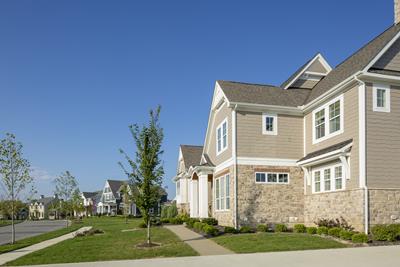 Eversole Run Neighborhood home with beige and a grey stone bottom half and beige siding top half of the foreground home. white trim with white enrty pillars, tree-lined streets and well-manicured lawns.