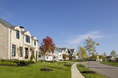 Eversole Run Neighborhood with a beige stone home with wooden pillars, well-manicured lawn with a red tree in the front yard ad tree-lined streets.