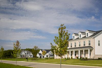 Eversole Run Neighborhood with a beige stone home with wooden pillars, well-manicured lawn with a red tree in the front yard ad tree-lined streets.